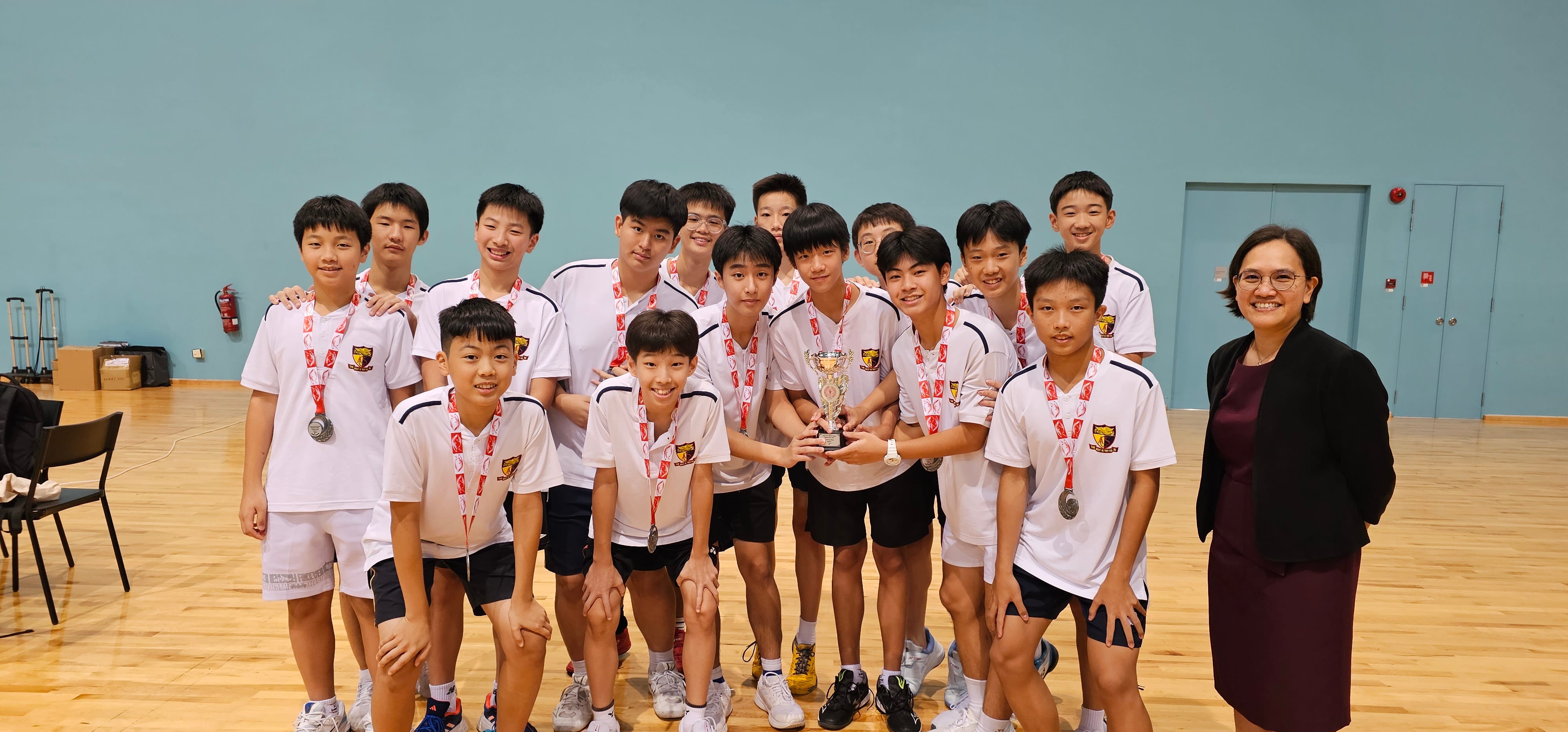 A school badminton team poses with medals alongside an adult official.
